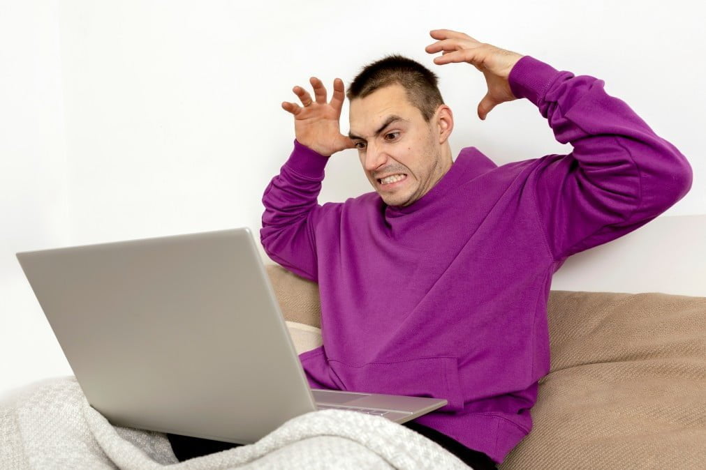 angry and dissatisfied man with violet hoodie sitting on bed with laptop computer man using notebook t20 pjp4gq